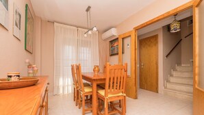 Un espace repas avec une table et des chaises en bois, un ventilateur de plafond et un escalier menant à l’étage supérieur.
