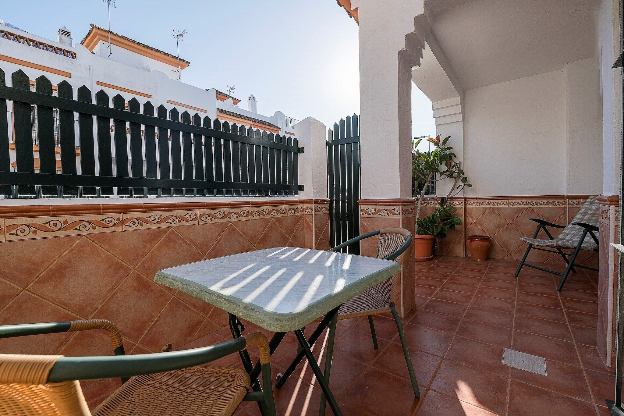A patio with a table and chairs, a black fence, and a potted plant.