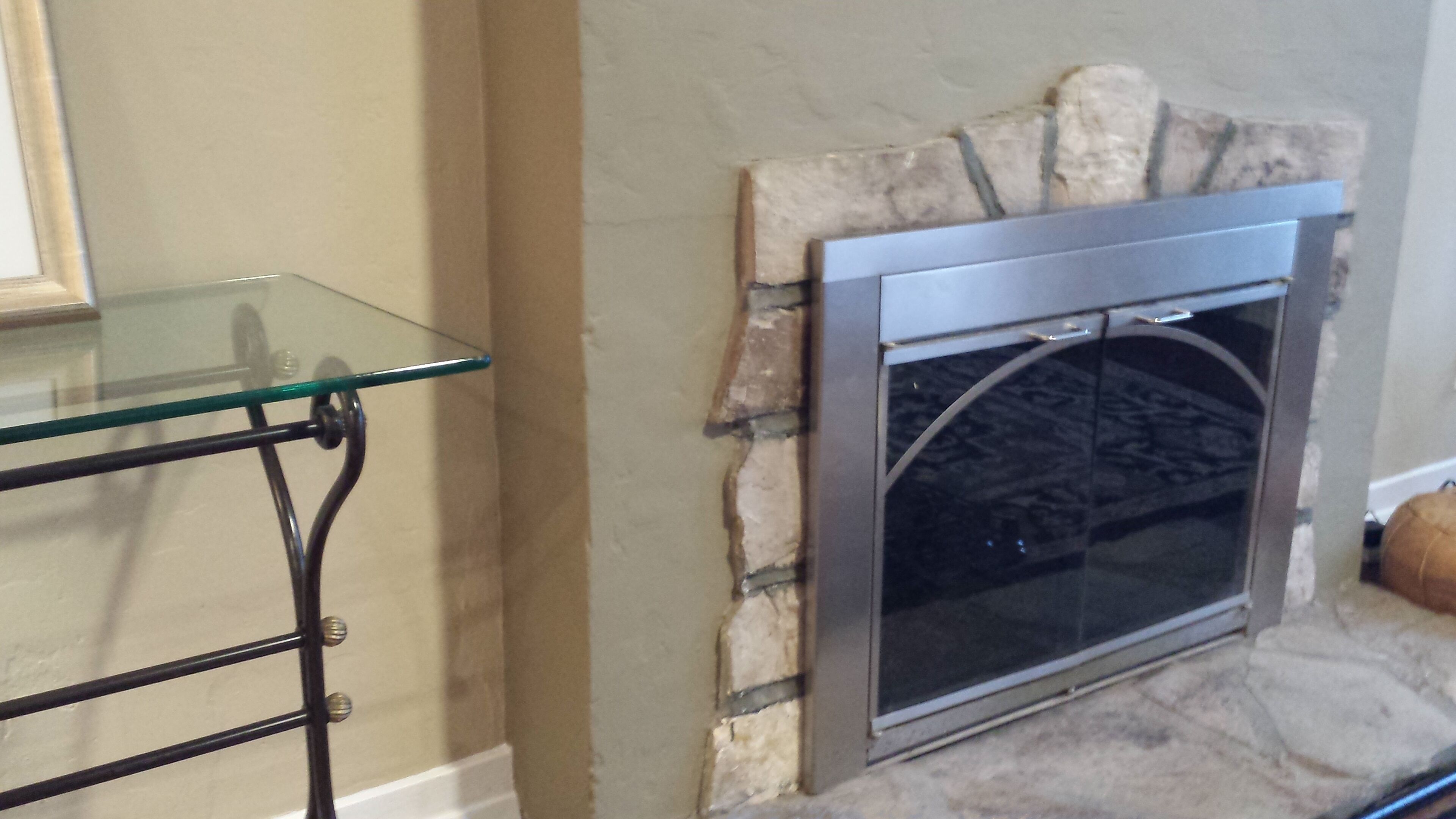 A fireplace with a stone surround and a glass shelf in front.