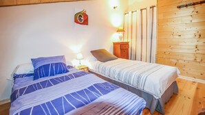 A room with two beds, wooden walls, a nightstand with a lamp, and a wall-mounted artwork. - Gorgeous home in Rochessauve with WiFi (Rochessauve)