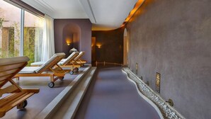 Een wellnessruimte met houten ligbedden, een pad met kiezelstenen en uitzicht op groen.