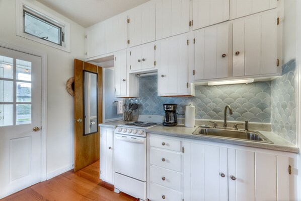 A kitchen with white cabinets, a stove, a sink, and a window.