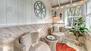 A cozy room with wicker furniture, a compass wall decoration, and a window with a view of trees.