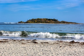A beach with waves approaching the shore and a small island in the distance.