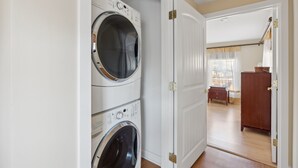 A laundry room with stacked washing machines and a door leading to a room with a wooden cabinet and a window. - RARE 3 Bedroom at the Resort at Goose Rocks Beach (Kennebunkport)
