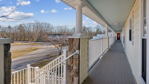 A covered porch with a stone column, a wooden railing, and a view of a road and trees. - RARE 3 Bedroom at the Resort at Goose Rocks Beach (Kennebunkport)