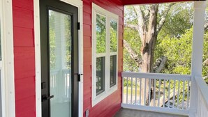 Eine überdachte Veranda mit roter Fassade, weißem Zierdekor und Blick auf Bäume und einen Zaun.