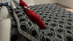 Ein Schlafzimmer mit einem schwarz-weiß gemusterten Bettbezug, einem roten Kopfkissen und einem wandmontierten Flachbildfernseher.