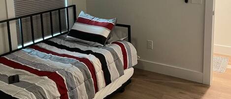 A bedroom with a bed, a television mounted on the wall, a window with blinds, and a door.