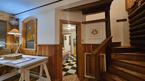 Een houten interieur met een trap, een bureau met een lamp en een lijst met een afbeelding aan de muur.