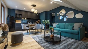 Una sala moderna con un sofá color turquesa, una mesa de centro de vidrio y un comedor con sillas, y una cocina al fondo.