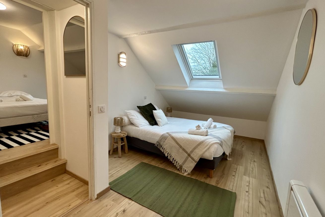 Una camera da letto con un letto, una finestra a lucernario, uno specchio e una scala.