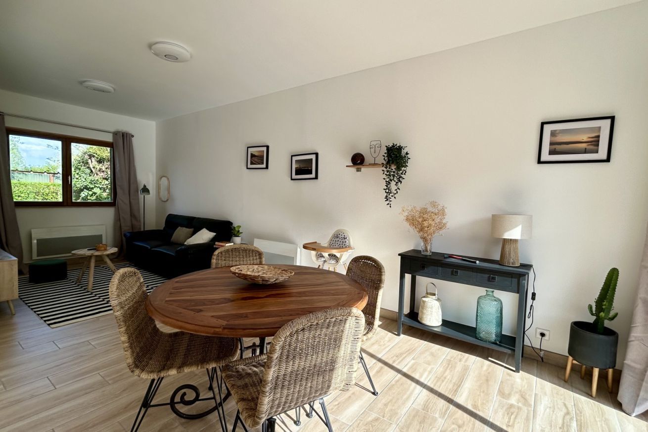 A living room with a round wooden table, wicker chairs, a black sofa, a small side table, a fireplace, and a window with curtains.