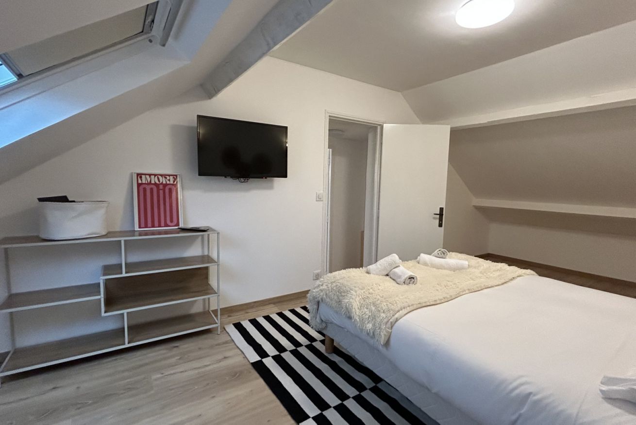 A bedroom with a bed, a TV mounted on the wall, a door, and a staircase.