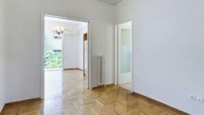 A spacious room with wooden flooring and white walls. There is a door leading to a balcony with a view of greenery.