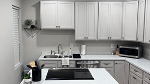 Une cuisine moderne avec des meubles blancs, un îlot central doté d’un plan de travail noir, deux tabourets de bar, un four à micro-ondes et un évier.