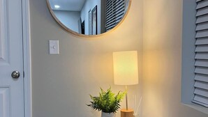 Un couloir avec un grand miroir rond, une petite table avec une lampe et une plante en pot.