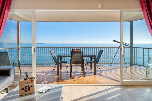 A balcony with a table, chairs, a bottle, and a box of chocolates.
