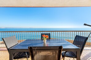 A table with chairs and a potted plant on a balcony overlooking the sea.