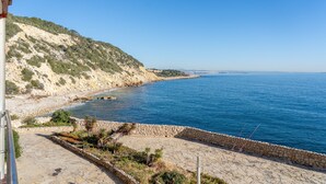 Une vue sur la côte, avec un sentier de pierres menant à la mer, une colline rocheuse et un ciel bleu dégagé.