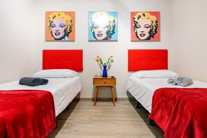 A hotel room with two beds, red headboards, white bedding, and three pop art paintings on the wall.
