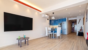 Un salon moderne doté d’un téléviseur à écran plat, d’un coin repas avec des chaises et d’une cuisine en arrière-plan.