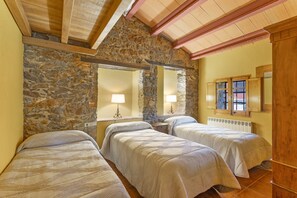 A room with three beds, stone walls, wooden beams, and a window with shutters.