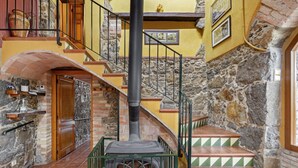 Eine Steintreppe führt zu einer Holztür, ein Kamin mit Schornstein und ein Fliesenboden sind zu sehen.