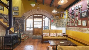 Ein gemütlicher Innenraum mit Kamin aus Stein, einer Holztreppe, einer Couch mit Kissen und einer Wand, die mit gerahmten Bildern geschmückt ist.