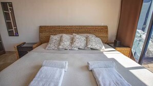 Un lit avec une tête de lit en osier, du linge de lit blanc et des coussins à motifs floraux.
