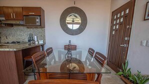 Un coin repas avec une table en verre, des chaises en bois, un four à micro-ondes et un miroir décoratif au mur.