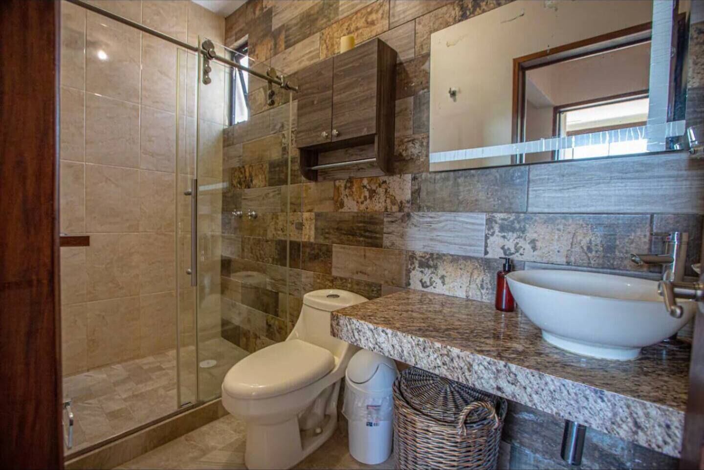A bathroom with a glass-enclosed shower, a toilet, a sink, and a mirror above the sink.
