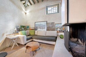 Un salon chaleureux avec un canapé d’angle, une petite table avec une lampe, une cheminée et des œuvres d’art accrochées aux murs.
