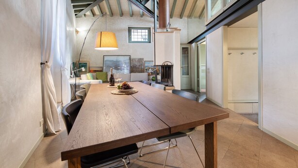 A dining area with a wooden table, chairs, a lamp, and a view of a kitchen and living area. - Holiday Apartment "Viasambuco" with Private Terrace & Wi-Fi (Iseo)