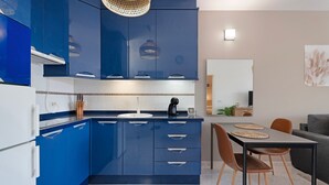 Et moderne køkken med blå skabe, et spisebord med stole, og en sofa i det tilstødende opholdsområde.