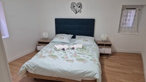 Un lit bien fait, avec une literie à motifs floraux, deux tables de chevet avec des lampes, un élément décoratif mural et une fenêtre avec un rideau.