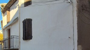 Un bâtiment à deux étages avec une porte de garage fermée, une petite fenêtre munie d’une grille métallique et un balcon avec une rambarde en métal.