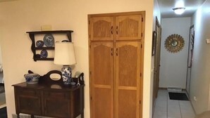 A room with a wooden wardrobe, a dark wooden dresser with a lamp, and a decorative mirror on the wall.