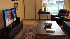 A living room with a television, a coffee table with a book and a bowl, a sofa, a door, and a window with blinds.
