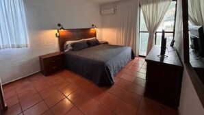Ein Schlafzimmer mit einem Bett, einem Nachttisch, einem Schreibtisch mit Computer und einem Fenster mit Vorhängen.