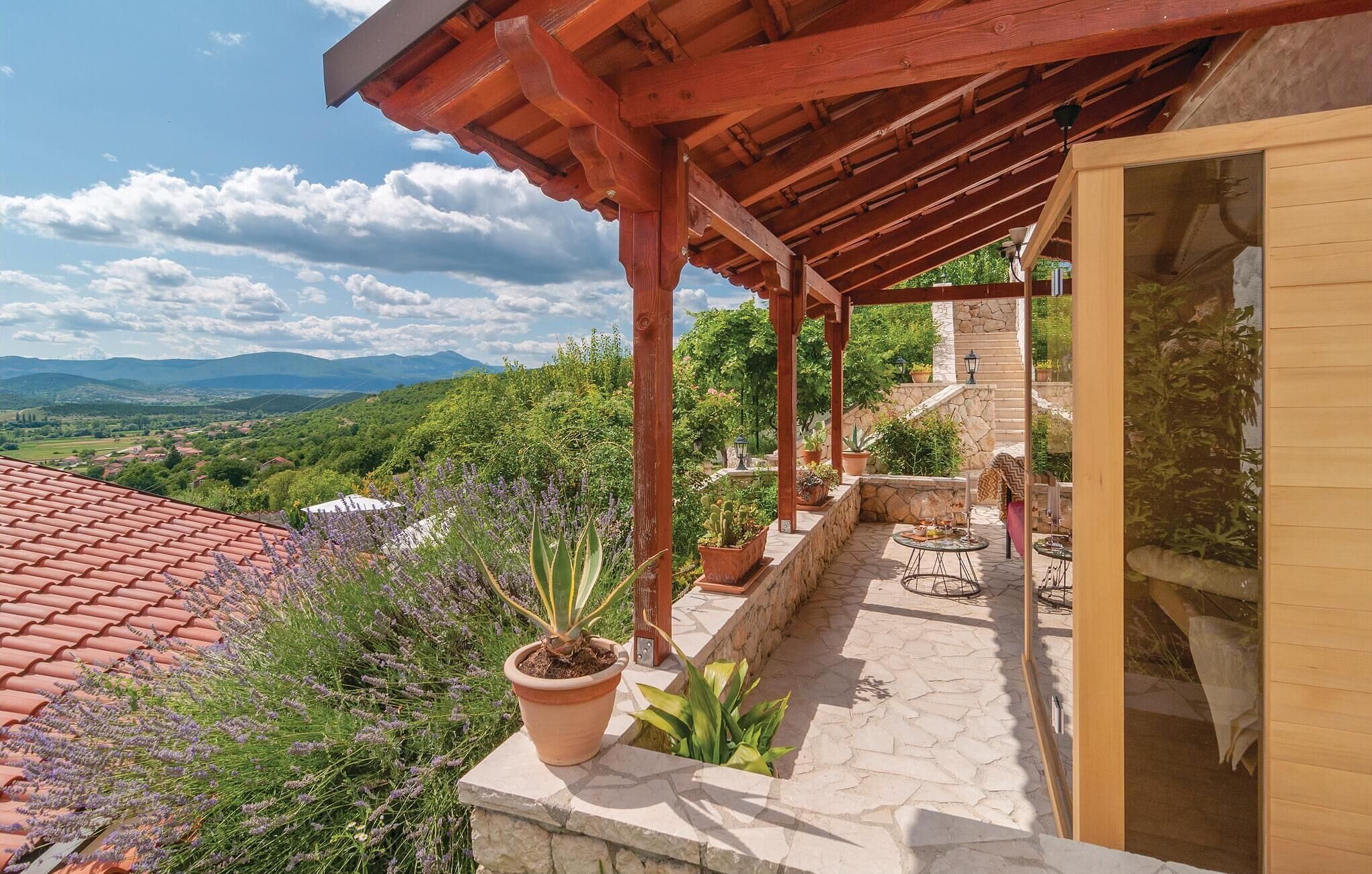 A covered outdoor area with a stone floor, potted plants, and a view of a mountainous landscape.