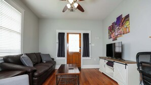 A living room with a brown leather sofa, a grey armchair, a wooden coffee table, a TV on a wooden stand, and a ceiling fan.