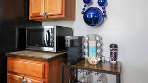 A kitchen with a microwave, coffee maker, and a small table with a coffee cup and a decorative blue beaded item.