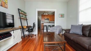 A modern living room with a brown leather sofa, a wooden coffee table, a TV on a cabinet, and a kitchen in the background.