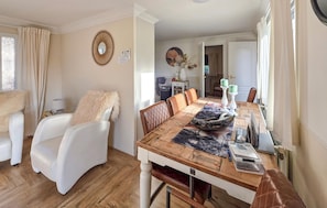 Un coin repas avec une table en bois, des chaises blanches et un miroir décoratif accroché au mur.