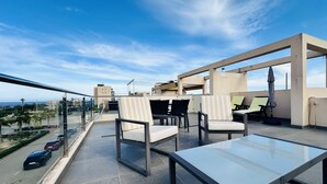 A rooftop terrace with a glass table and chairs, a view of the city, and a clear sky. - Apartamento Elisa (Torre de la Horadada) (Pilar de la Horadada)