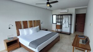 A modern hotel room with a large bed, a wooden nightstand, a desk with a laptop, a robe rack, and a ceiling fan.