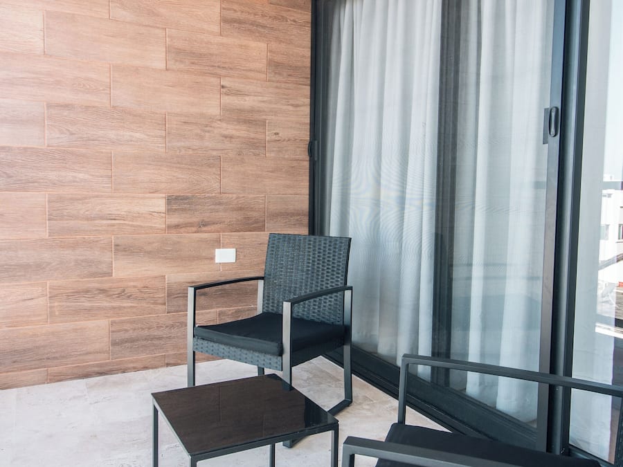 Een balkon met een houten wand, een stoel, een tafeltje en een groot raam met gordijnen.