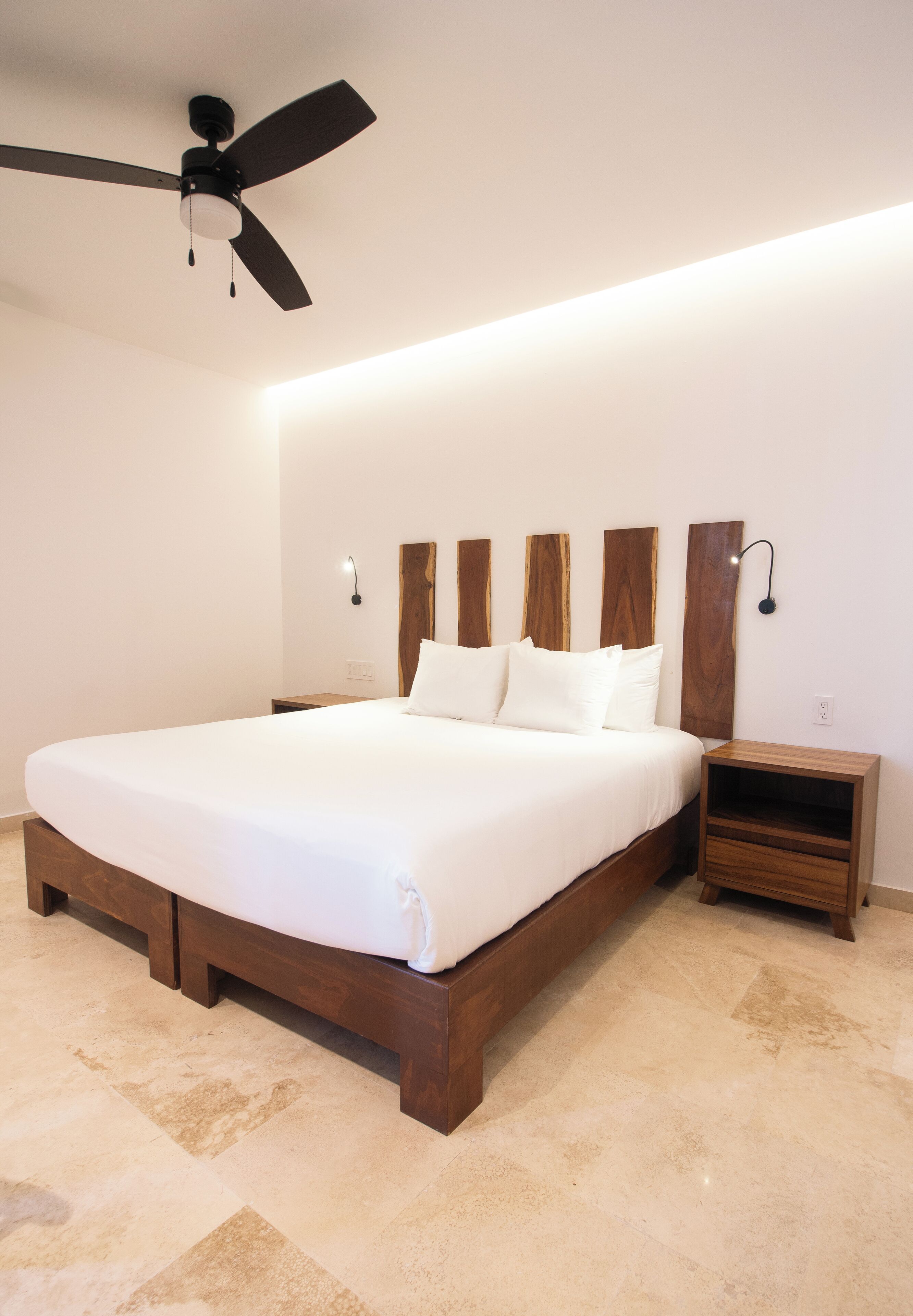 Un dormitorio con una cama grande, un ventilador de techo, una mesita de noche y un aplique de pared.