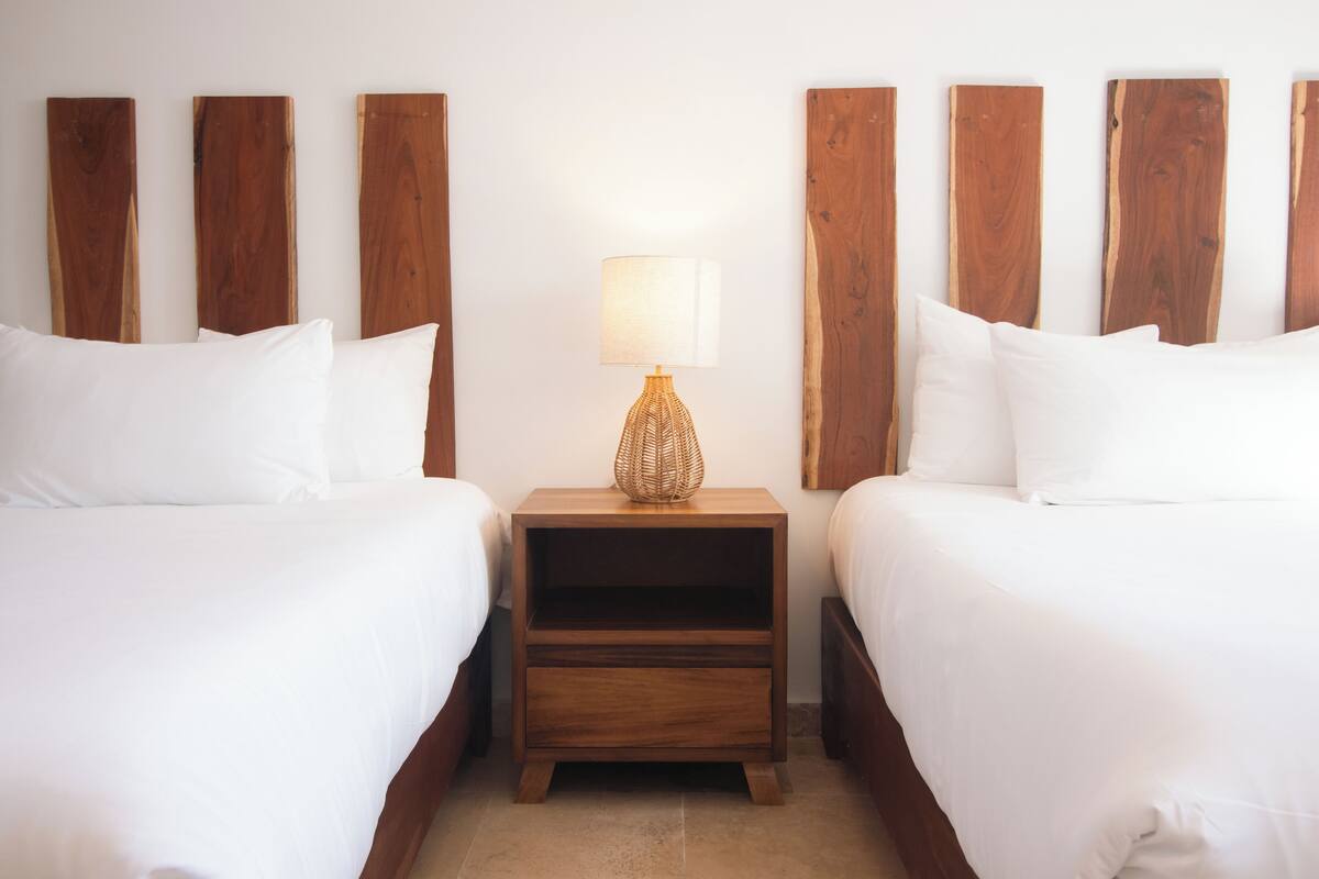 Ein Hotelzimmer mit zwei Betten, einem Nachttisch aus Holz mit Lampe und Holz-Kopfteilen.